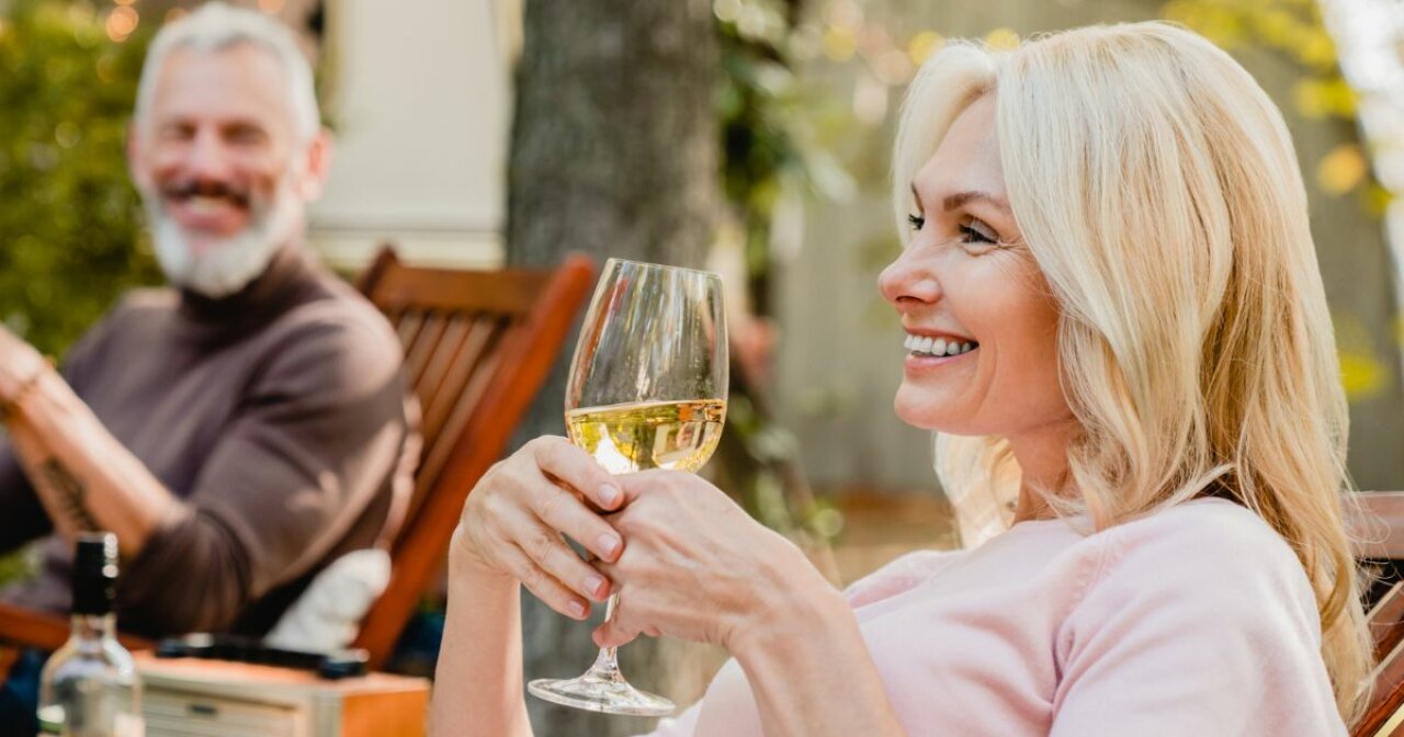 Happy older woman holding a glass of wine sitting with her  husband in the garden